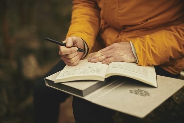 Person holding a pen and writing in a note book